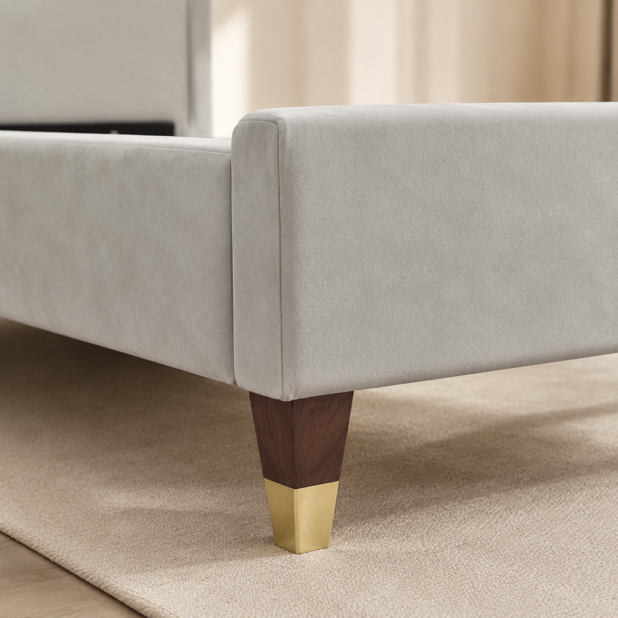 Close view of RANIYA's light grey suede footboard and gold-capped dark wooden leg