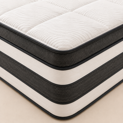 A close-up of a mattress corner showing a quilted white top surface, dark charcoal side panels, and cream-colored horizontal stripes, set against a light beige background.