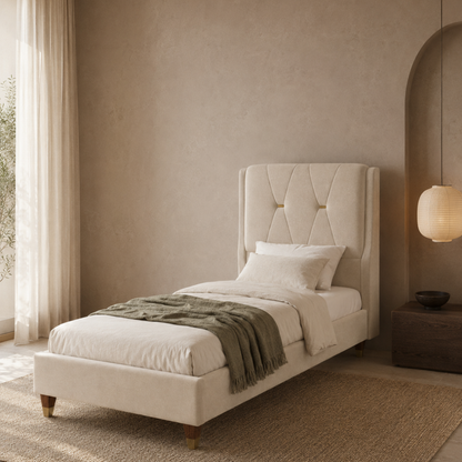 A single bed with a tall tufted upholstered headboard in a warm cream or off-white fabric, styled with white bedding, a textured olive green throw blanket, and wooden legs, set in a minimalist beige bedroom.