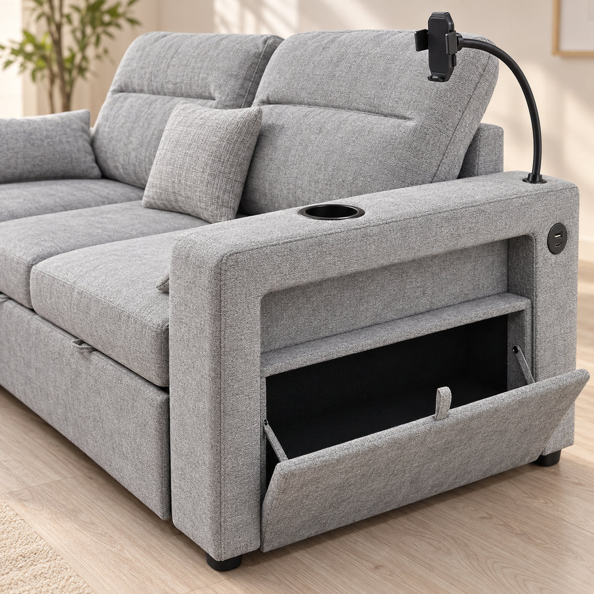 A light gray fabric reclining sofa shown in a bright indoor room, with the front storage compartment open and a black flexible phone stand attached over the backrest.